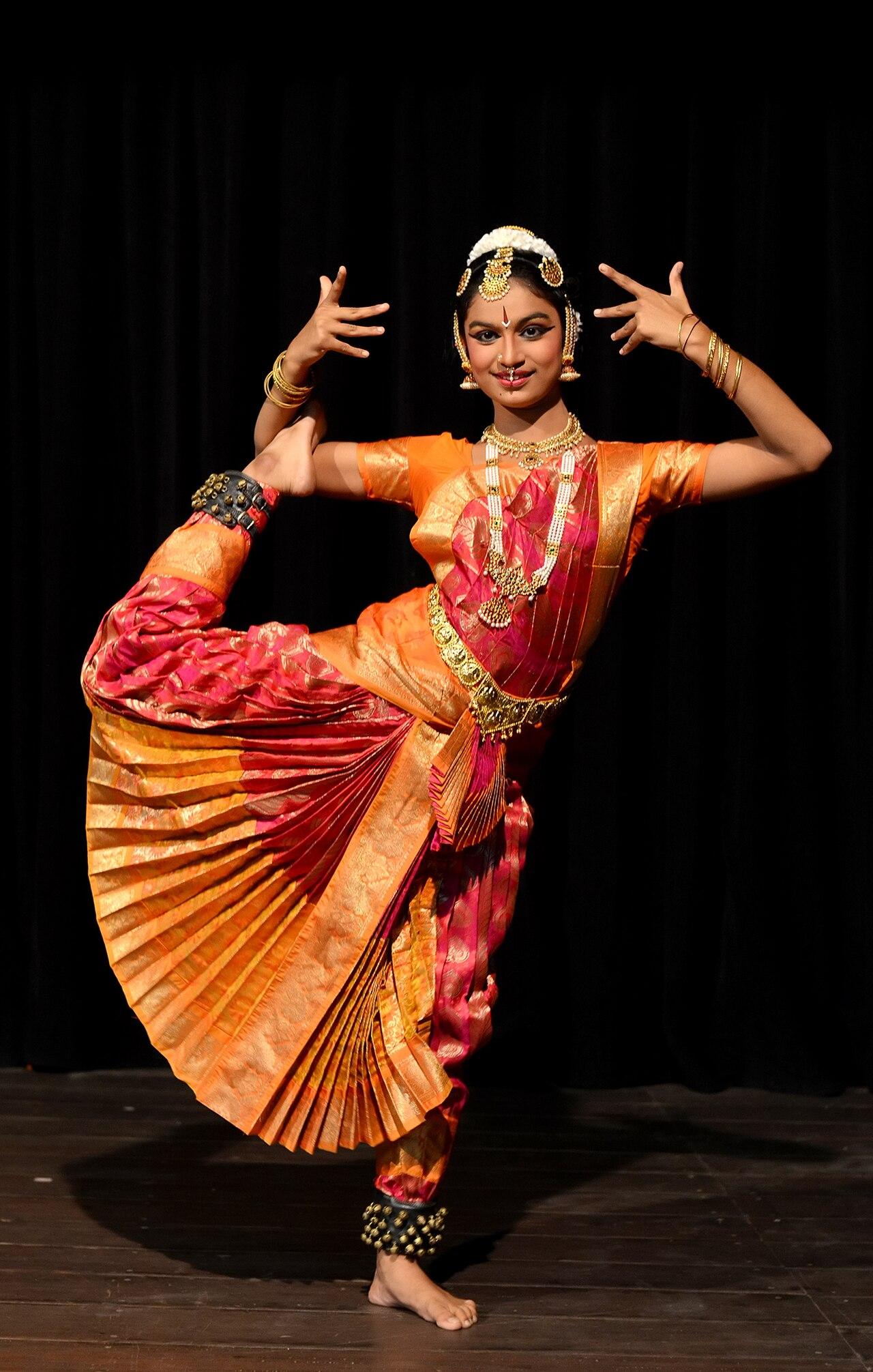 Bharatanatyam dancer holding a classical pose in a traditional orange costume