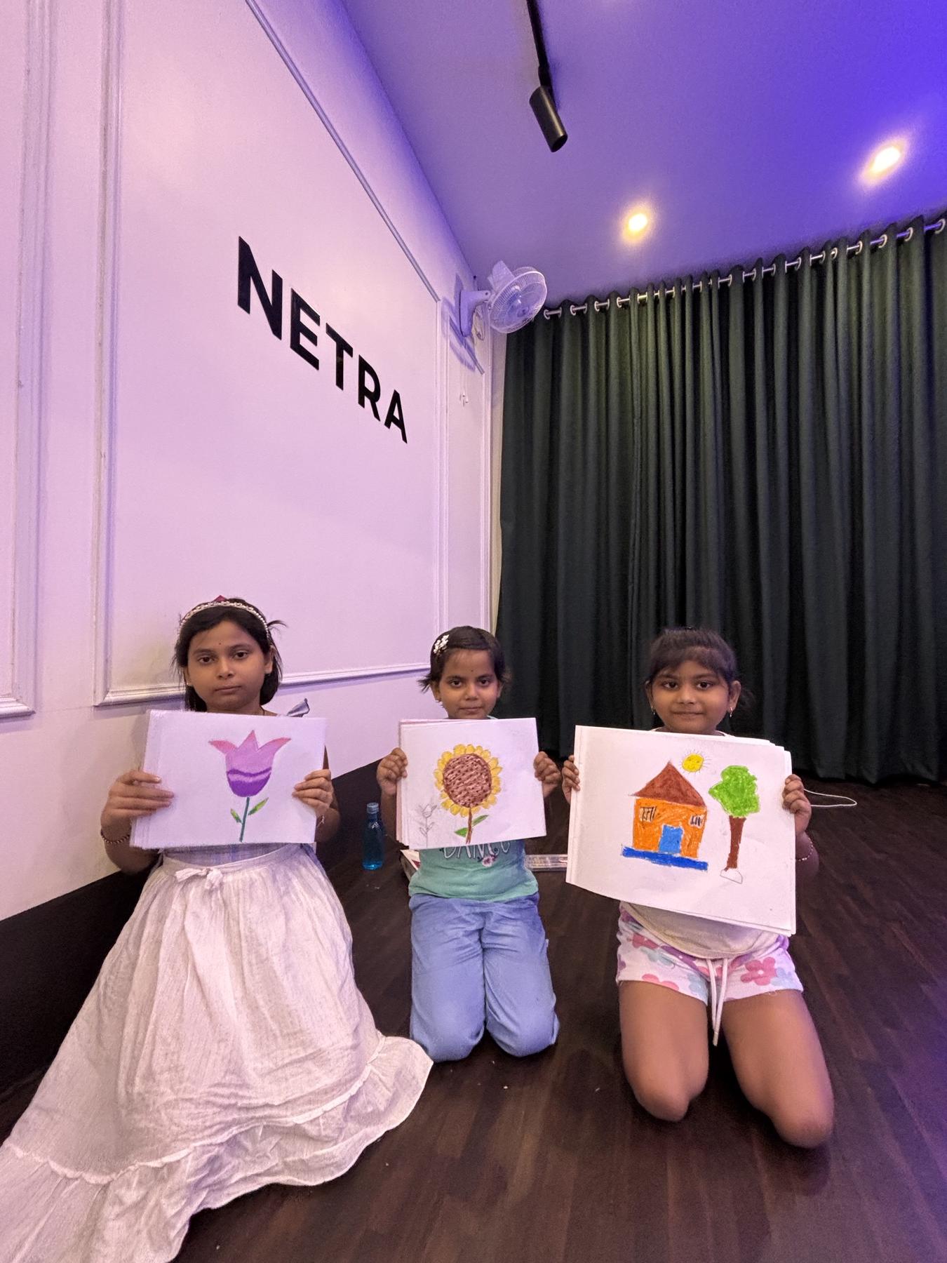 Three young students proudly holding up their drawings of a flower, a sunflower and a house