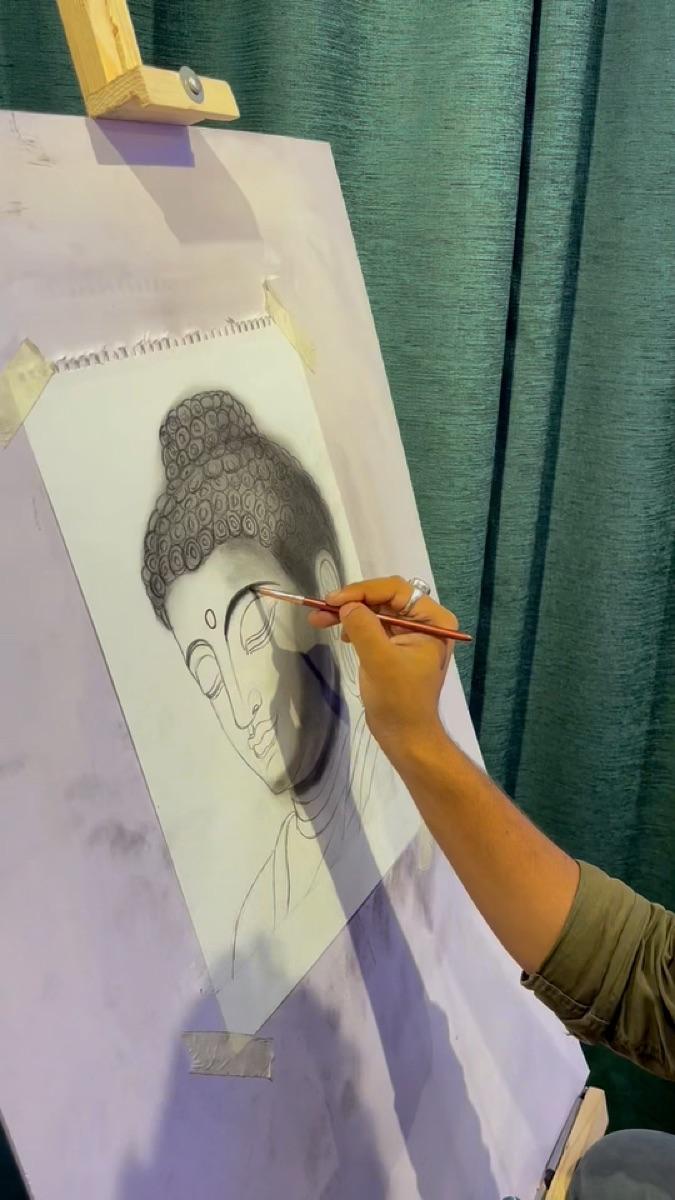 Artist sketching a portrait of the Buddha on an easel