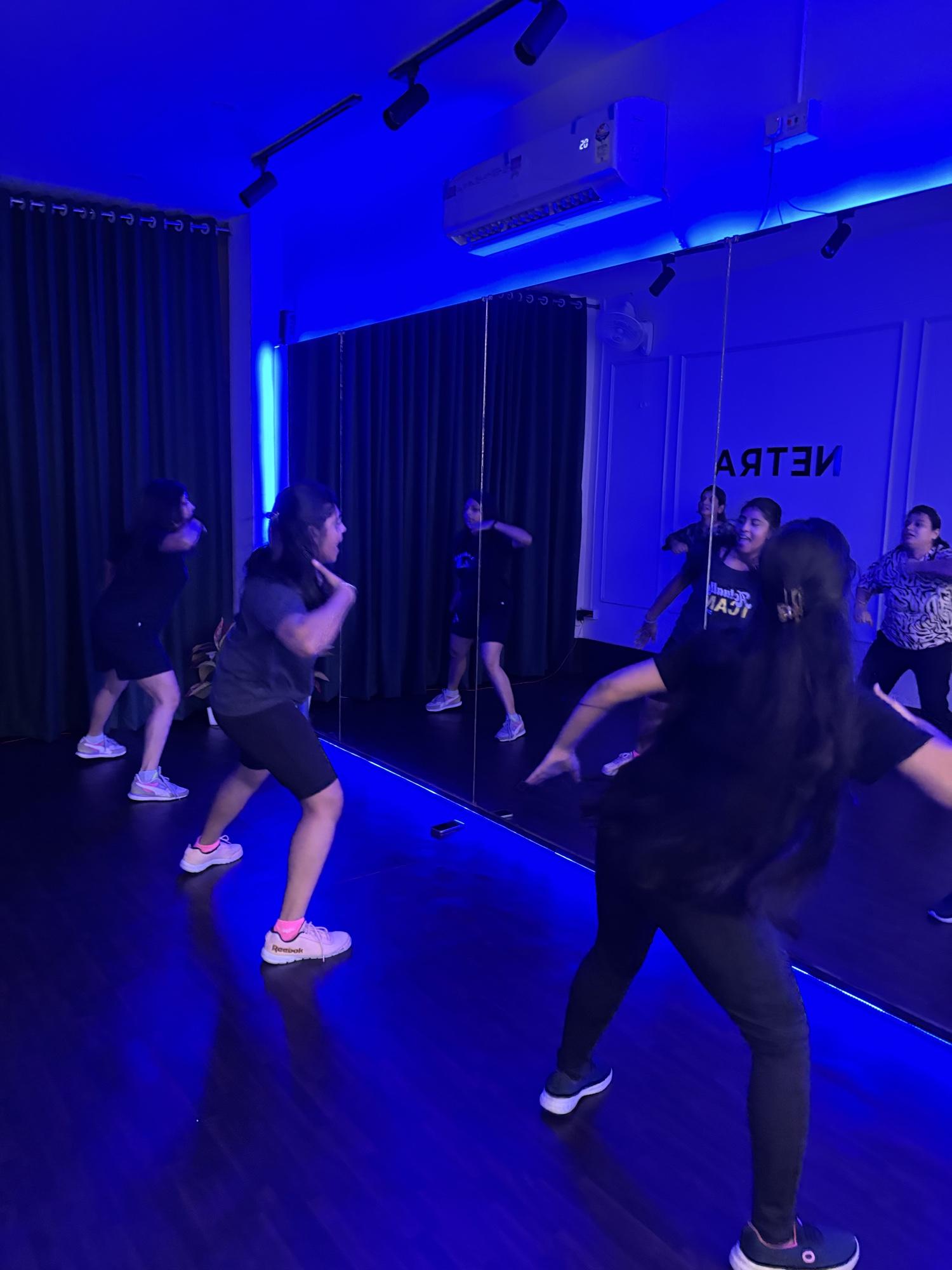 Zumba class dancing in front of the studio mirror under blue lights at Netra
