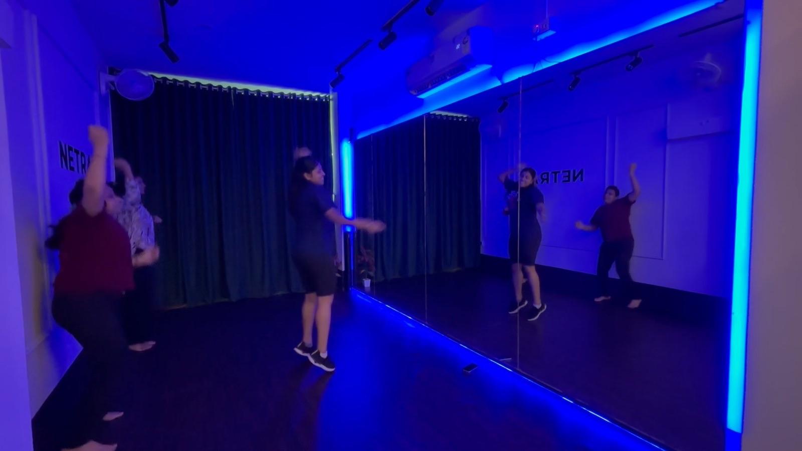 Zumba class with arms raised, dancing across the blue-lit Netra studio