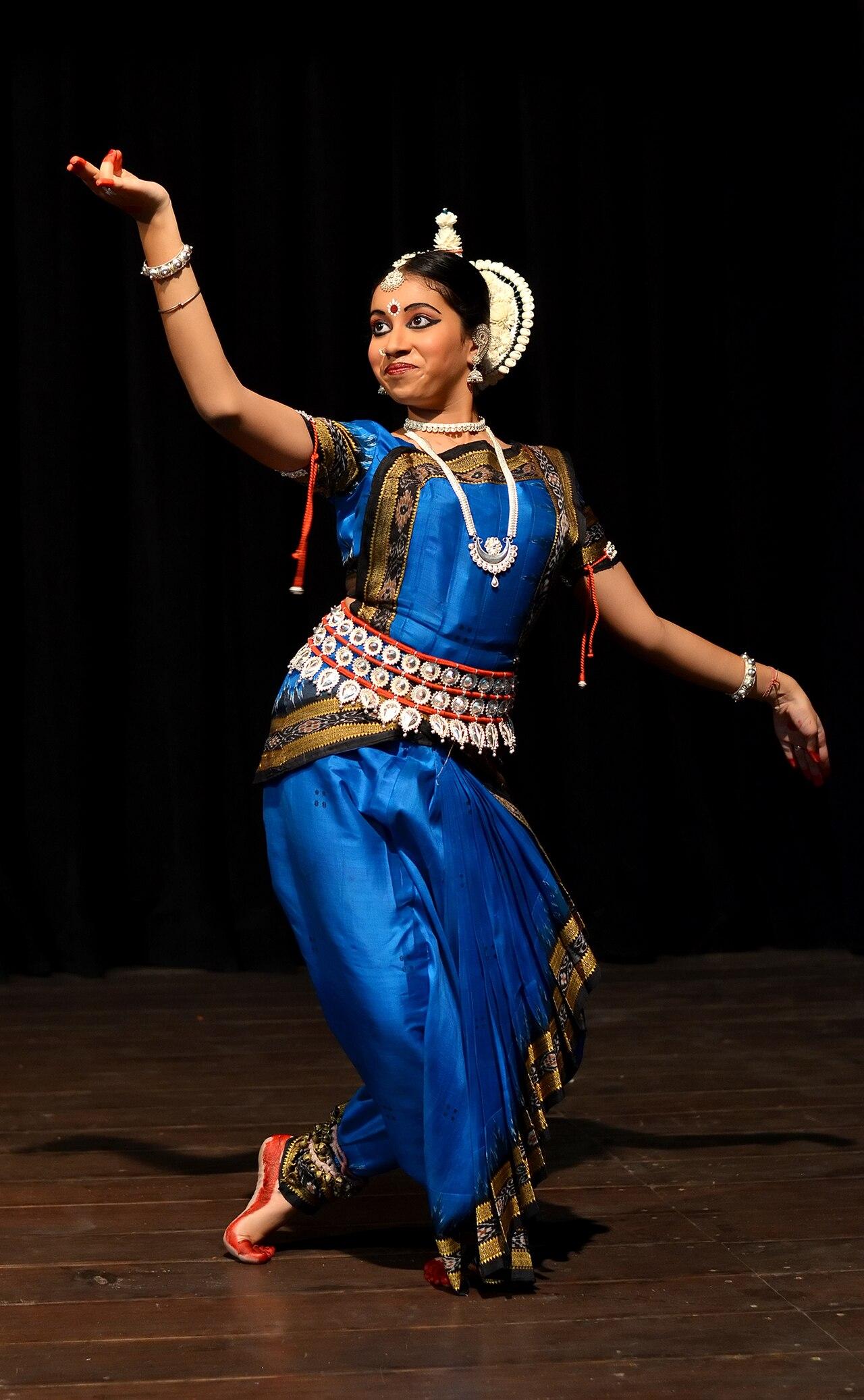 Odissi dancer in a graceful tribhangi pose wearing a blue costume