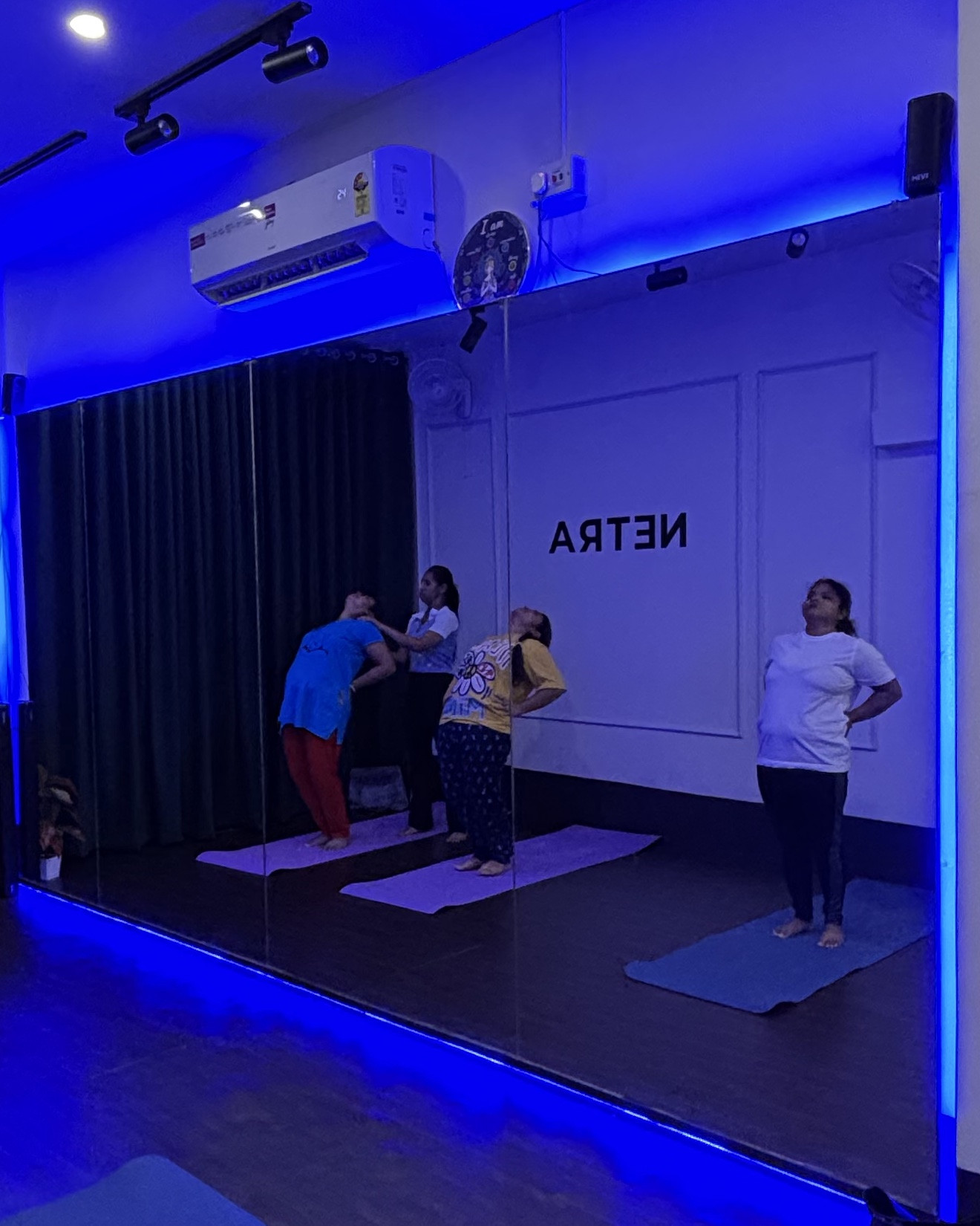 Yoga class reflected in the studio mirror, stretching together under soft blue light